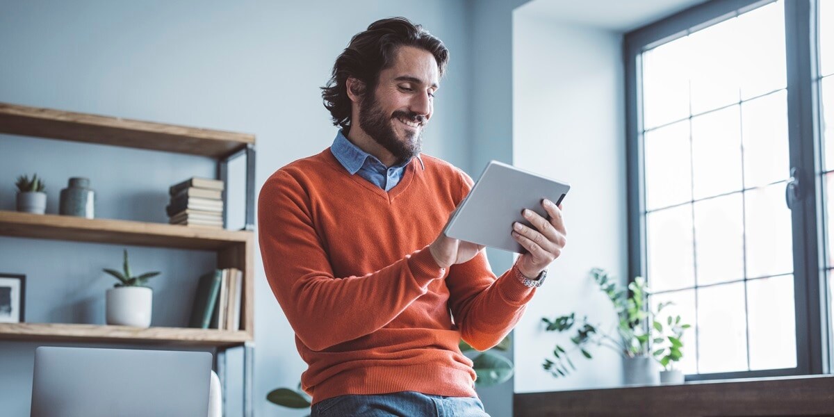 Man in an orange sweater looking at a hand held computer