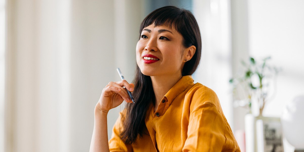 smiling woman sitting at a table, holding pen in hand