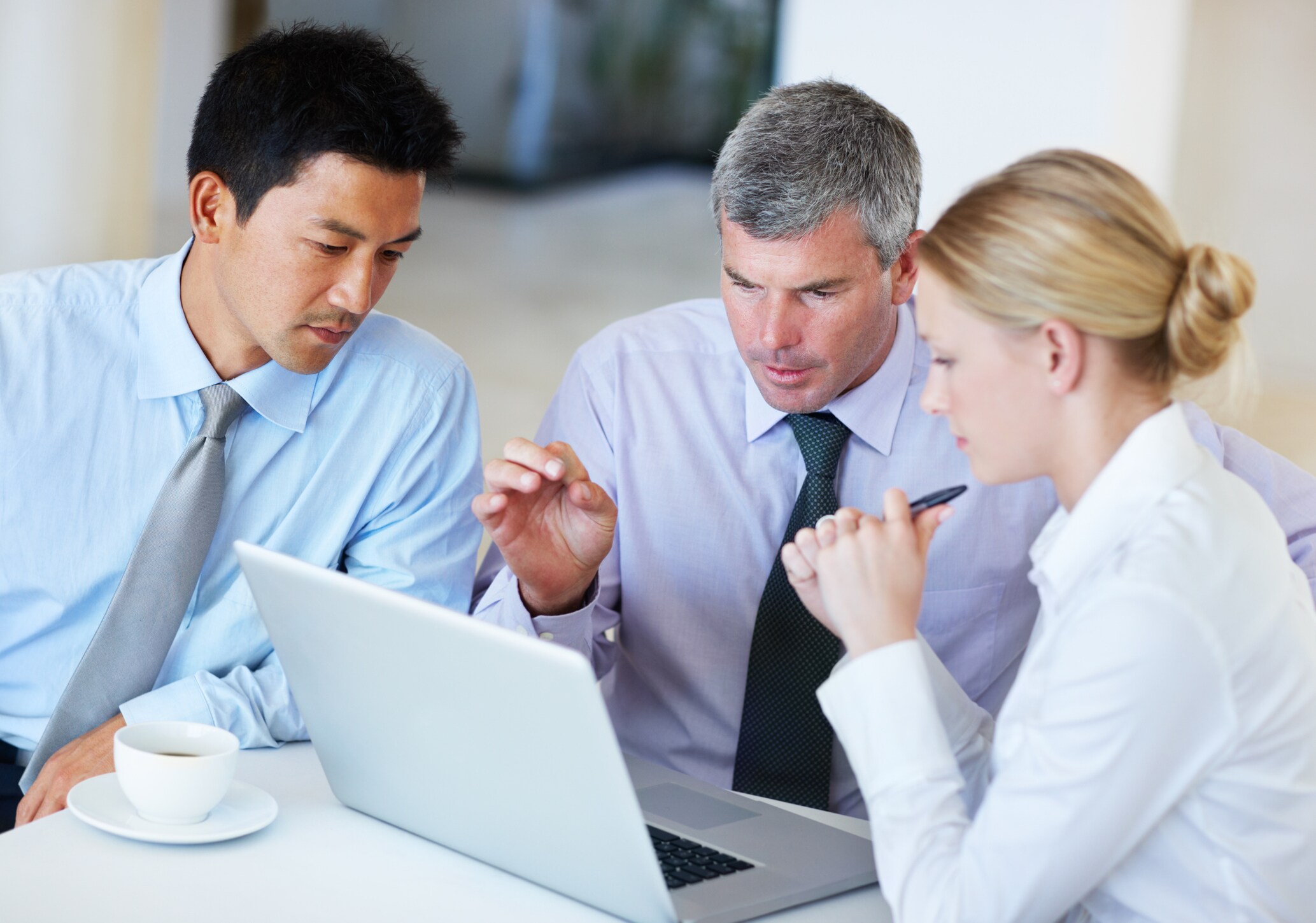 two men and one woman looking at laptop in office setting