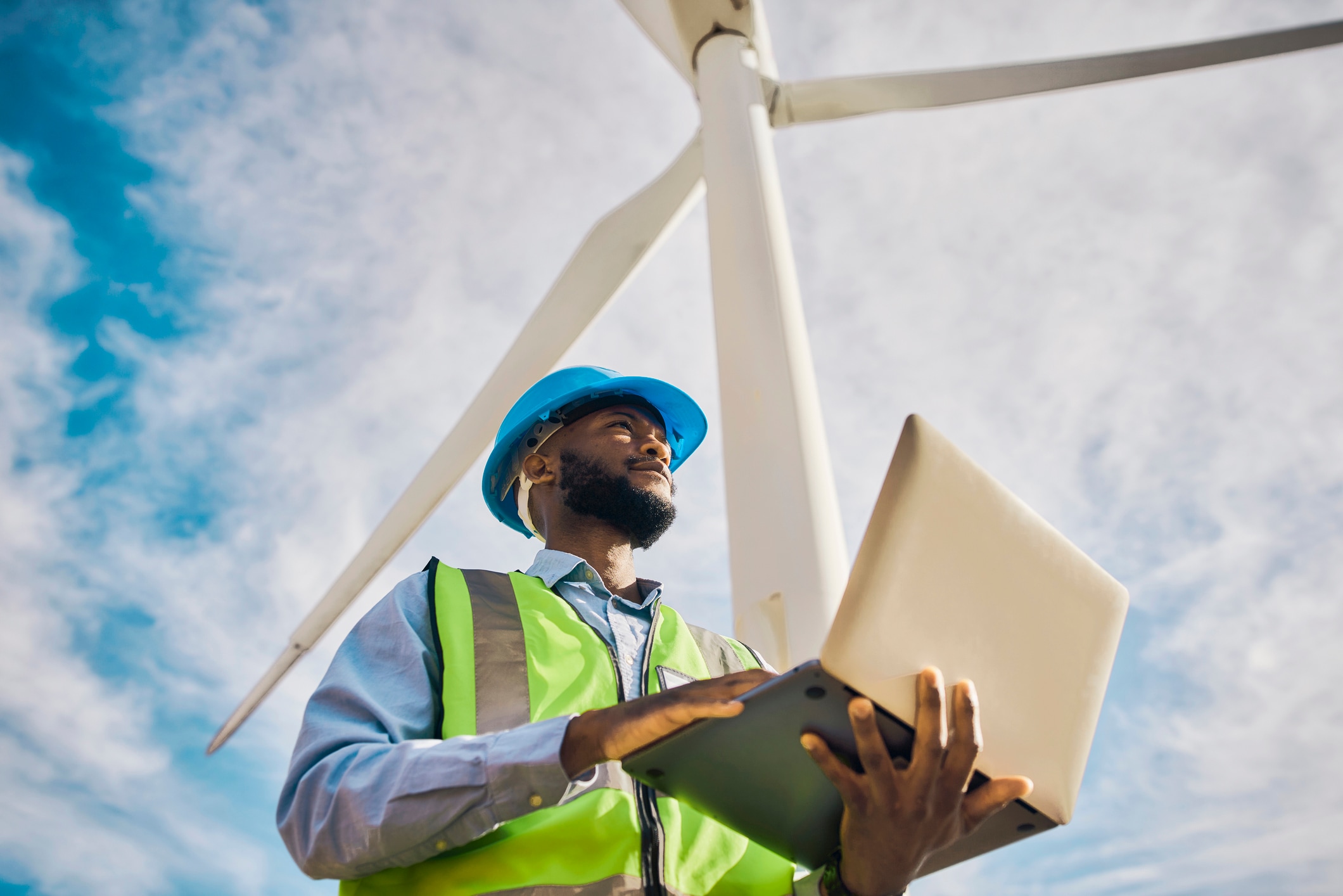 Man at a windmill energy plant using a tablet and looking out