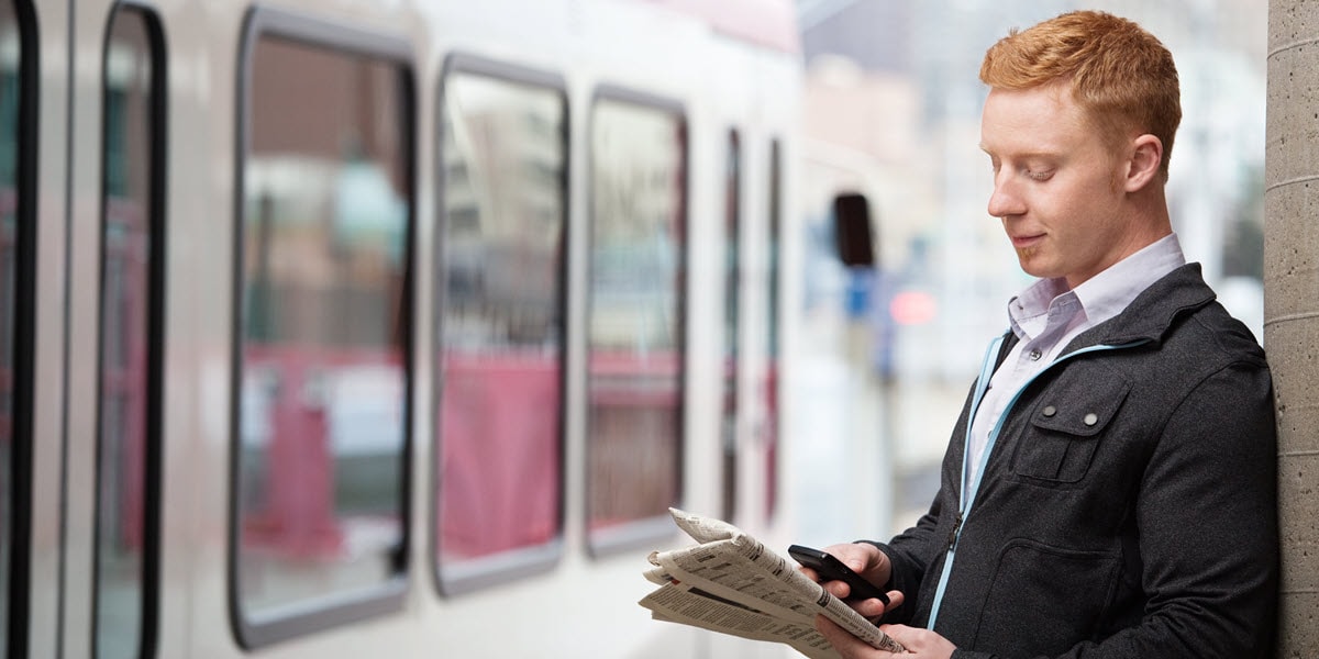 man standing next to train holding newspaper and cell phone