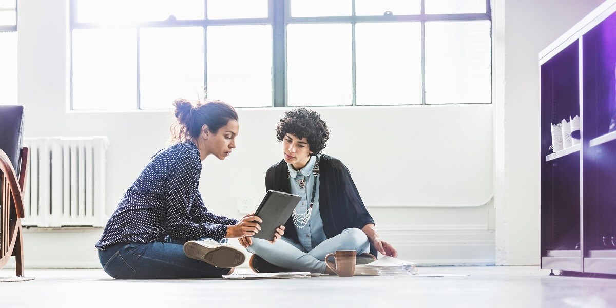 Two people sitting on a floor looking at a tablet together