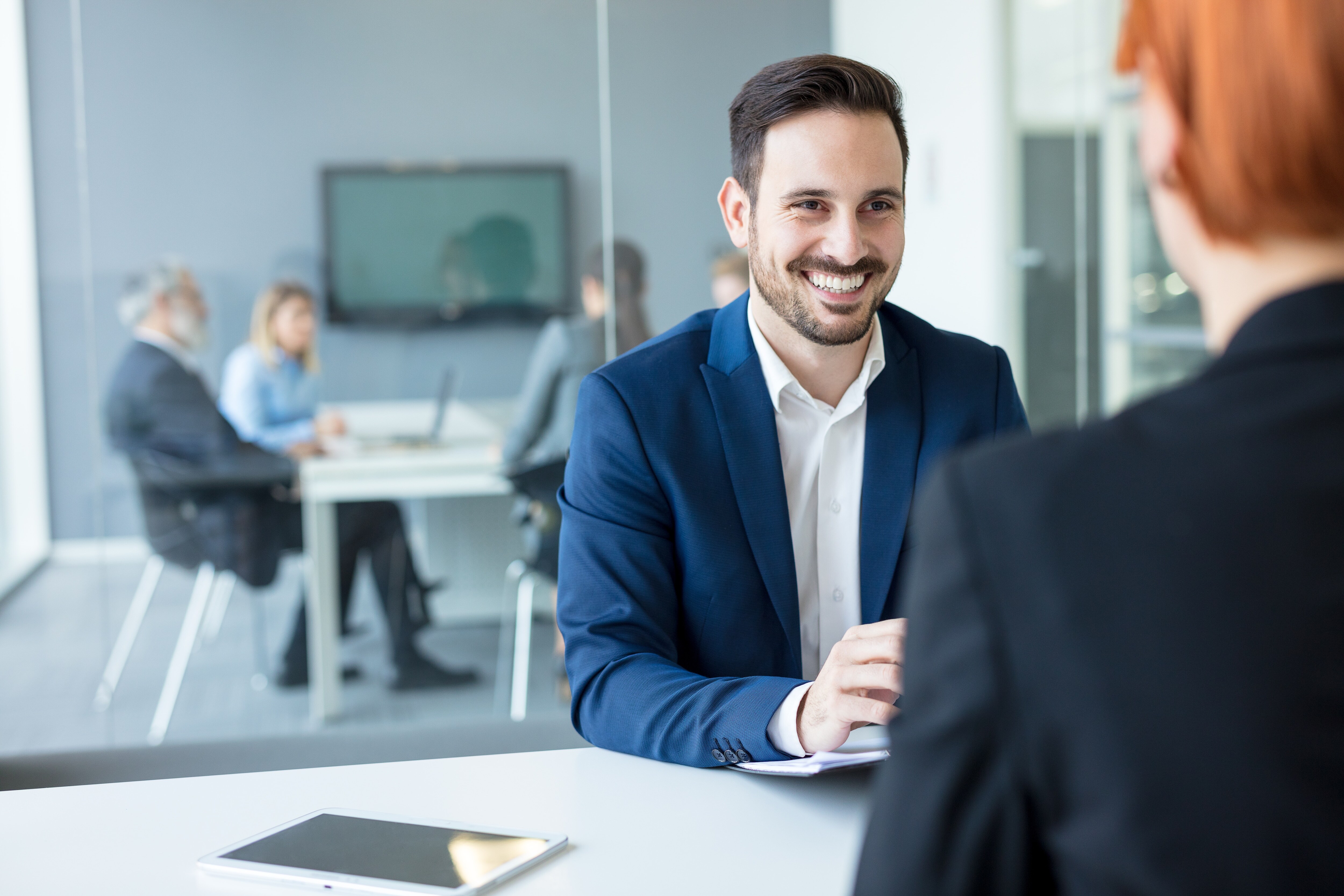 Man sitting at a table in a suit smiling at someone else 