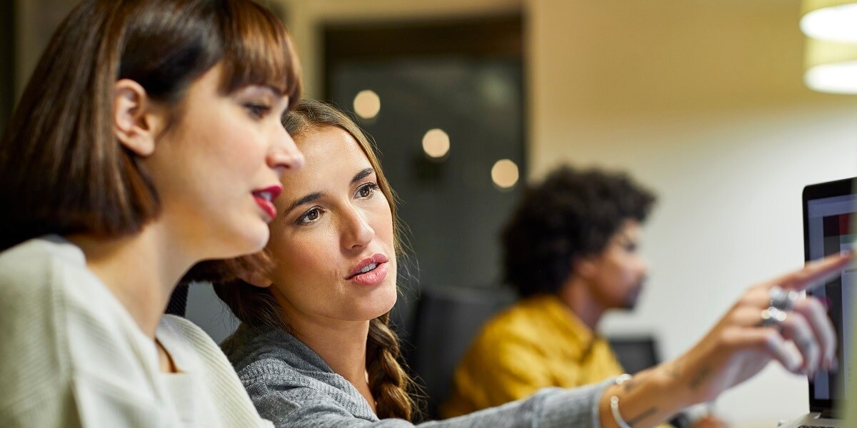 Two office workers looking over a laptop computer.