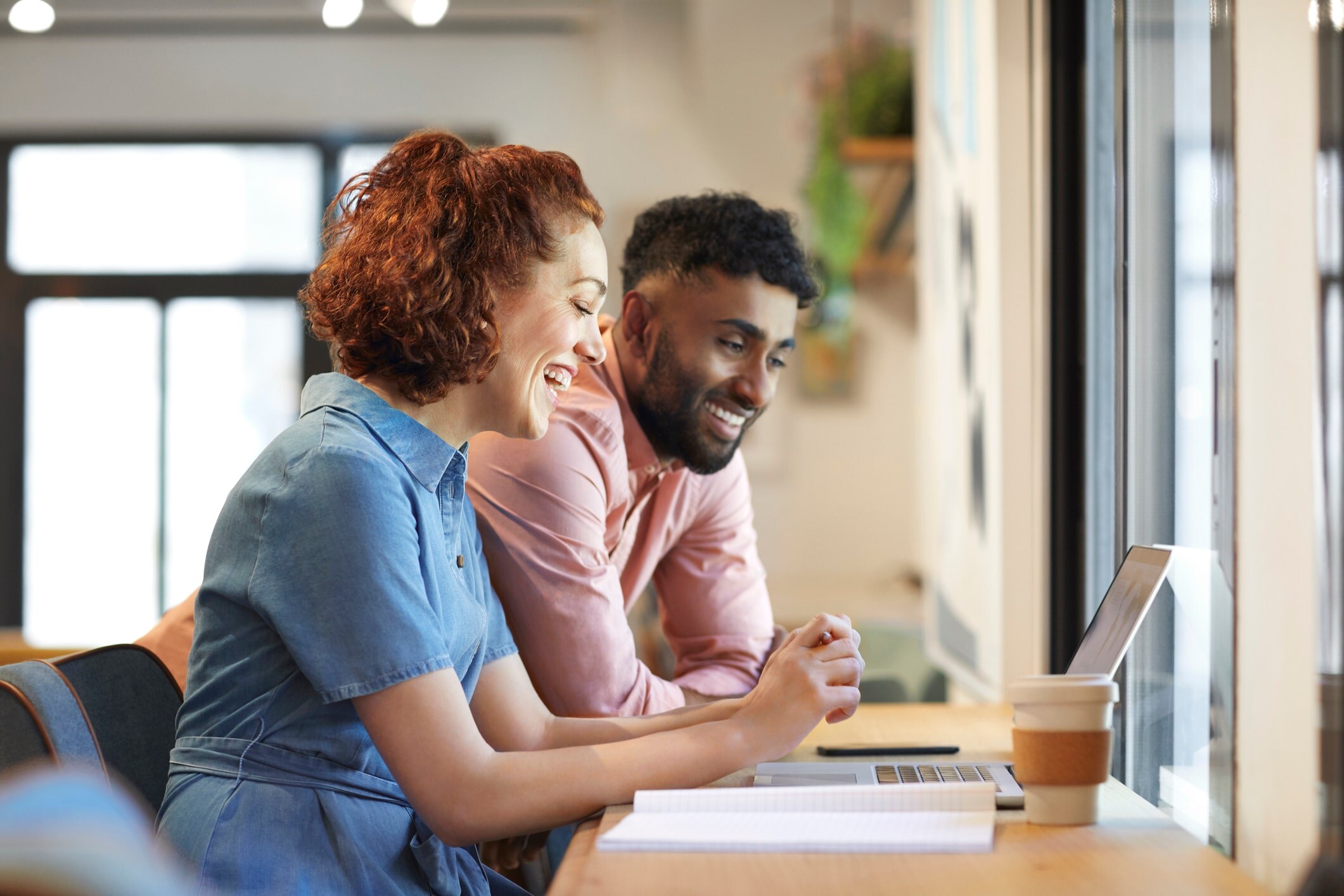 man standing, woman sitting, smiling at laptop