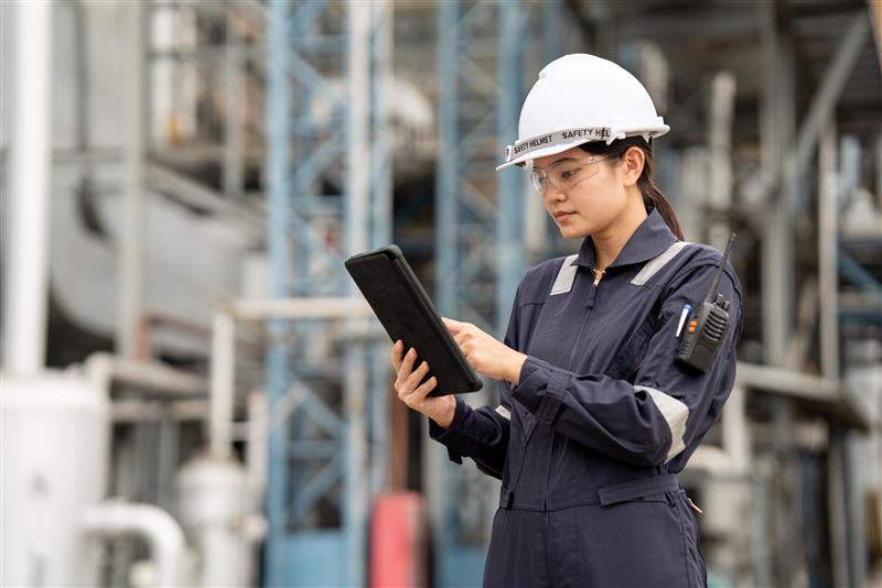 Woman working in utilities wearing a hard hat and looking at a tablet