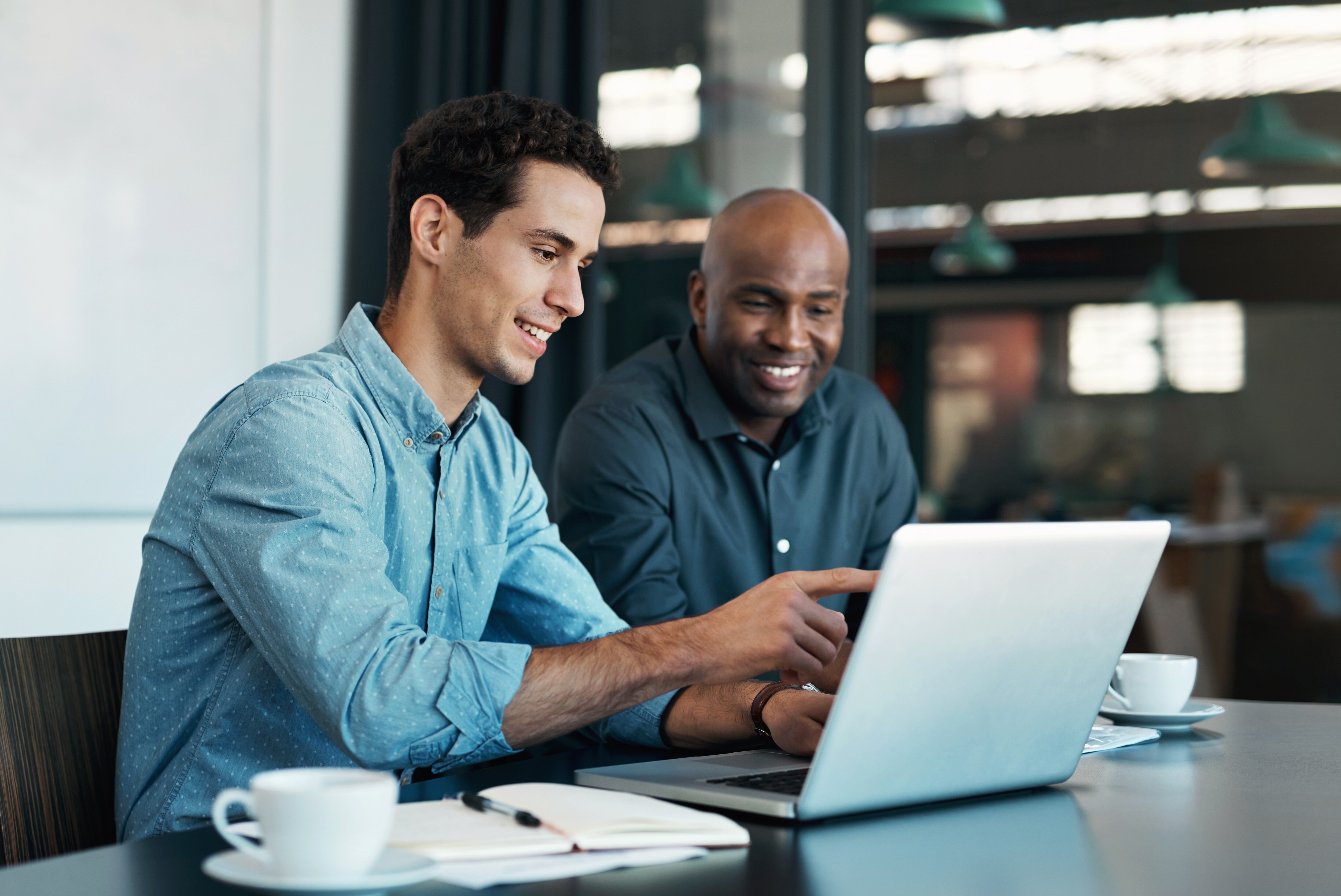Two diverse men sitting, talking to each other something on their computer