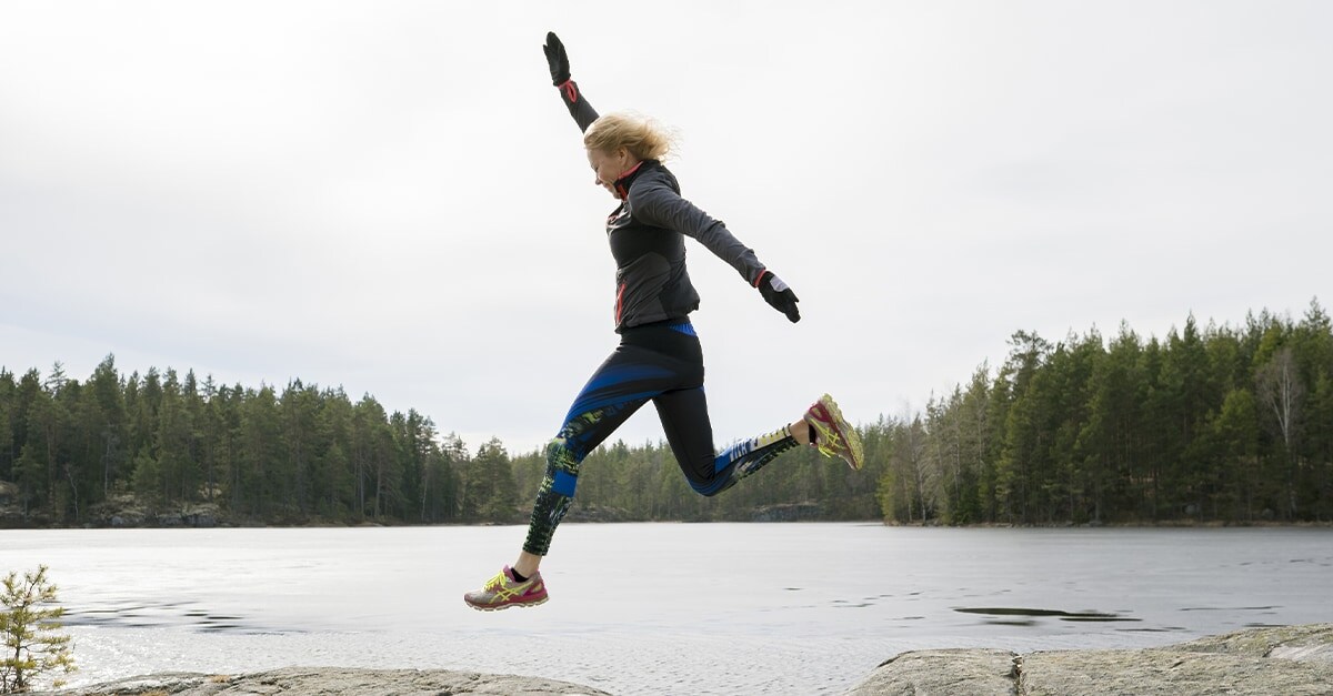 Woman jumping between two large rocks next to a body of water