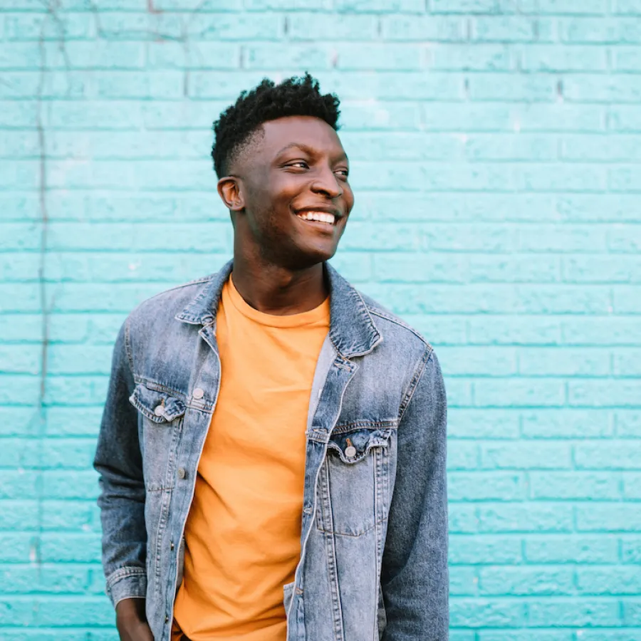 Cheerful man smiling in front of a teal brick wall