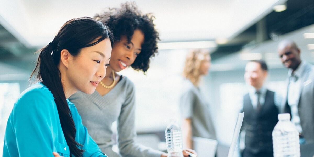 Two office workers looking over a laptop computer.